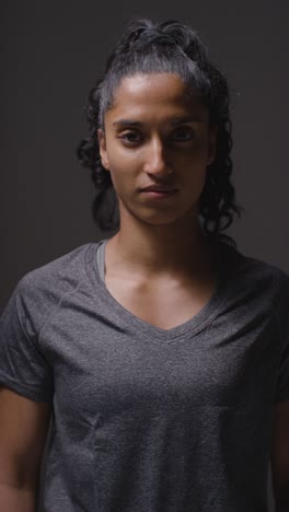 Vertical-Video-Studio-Shot-Of-Woman-Wearing-Sports-Clothing-Against-Dark-Background-Warming-Up-1